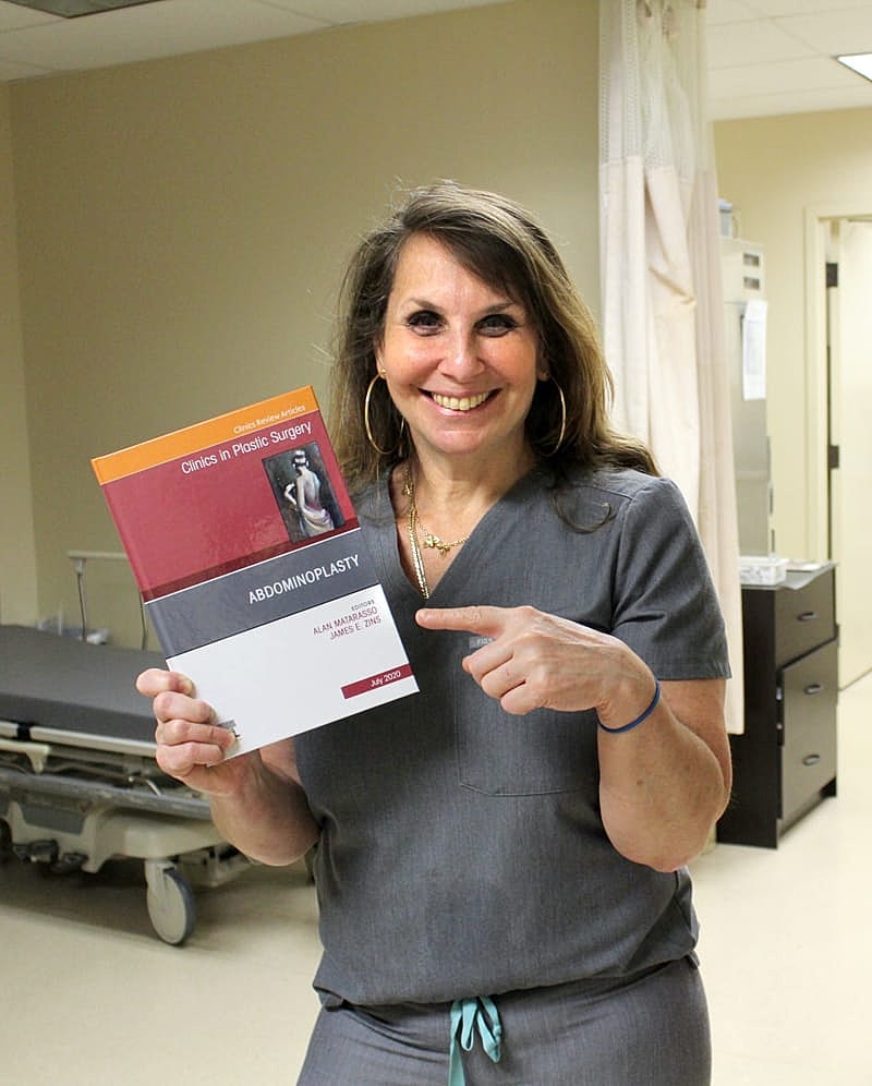 Smiling medical professional holding abdominal surgery book.