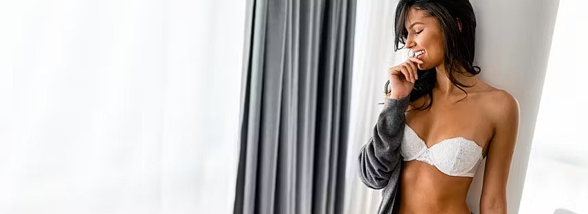 Woman in lingerie, smiling by window.