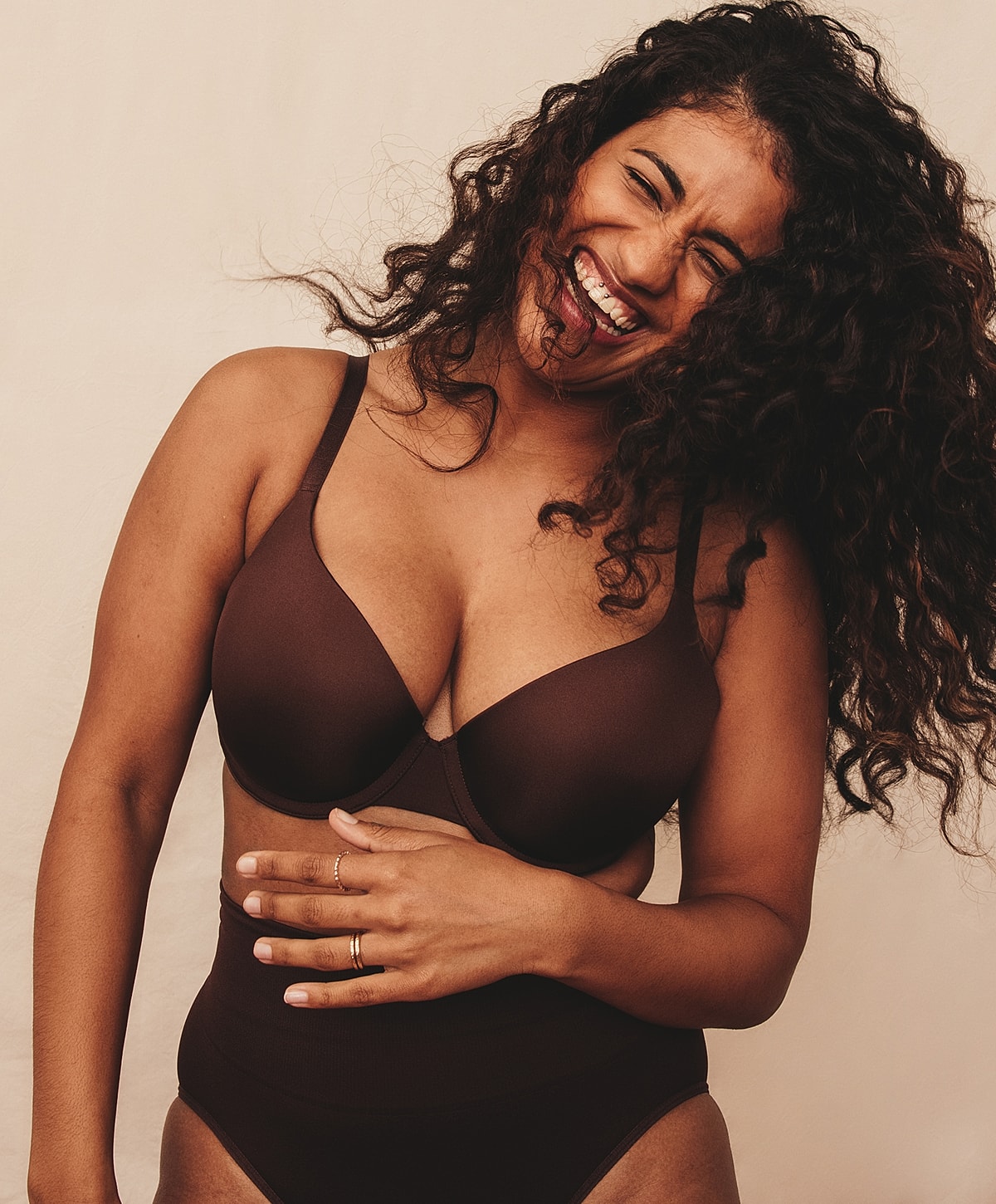 Smiling woman in brown lingerie, playful pose.