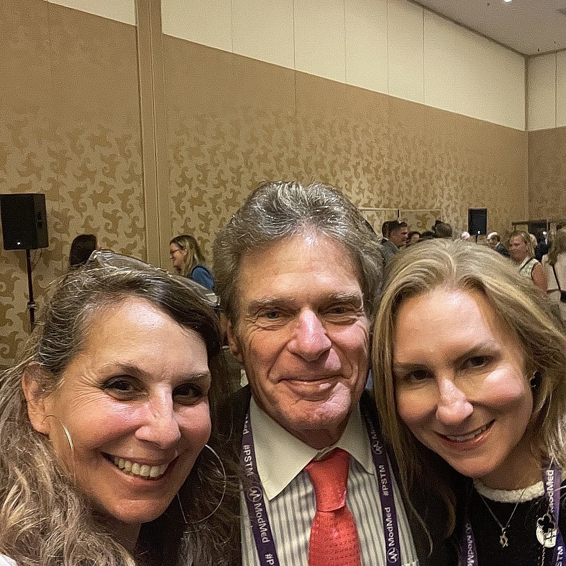 Three people smiling in a conference setting.