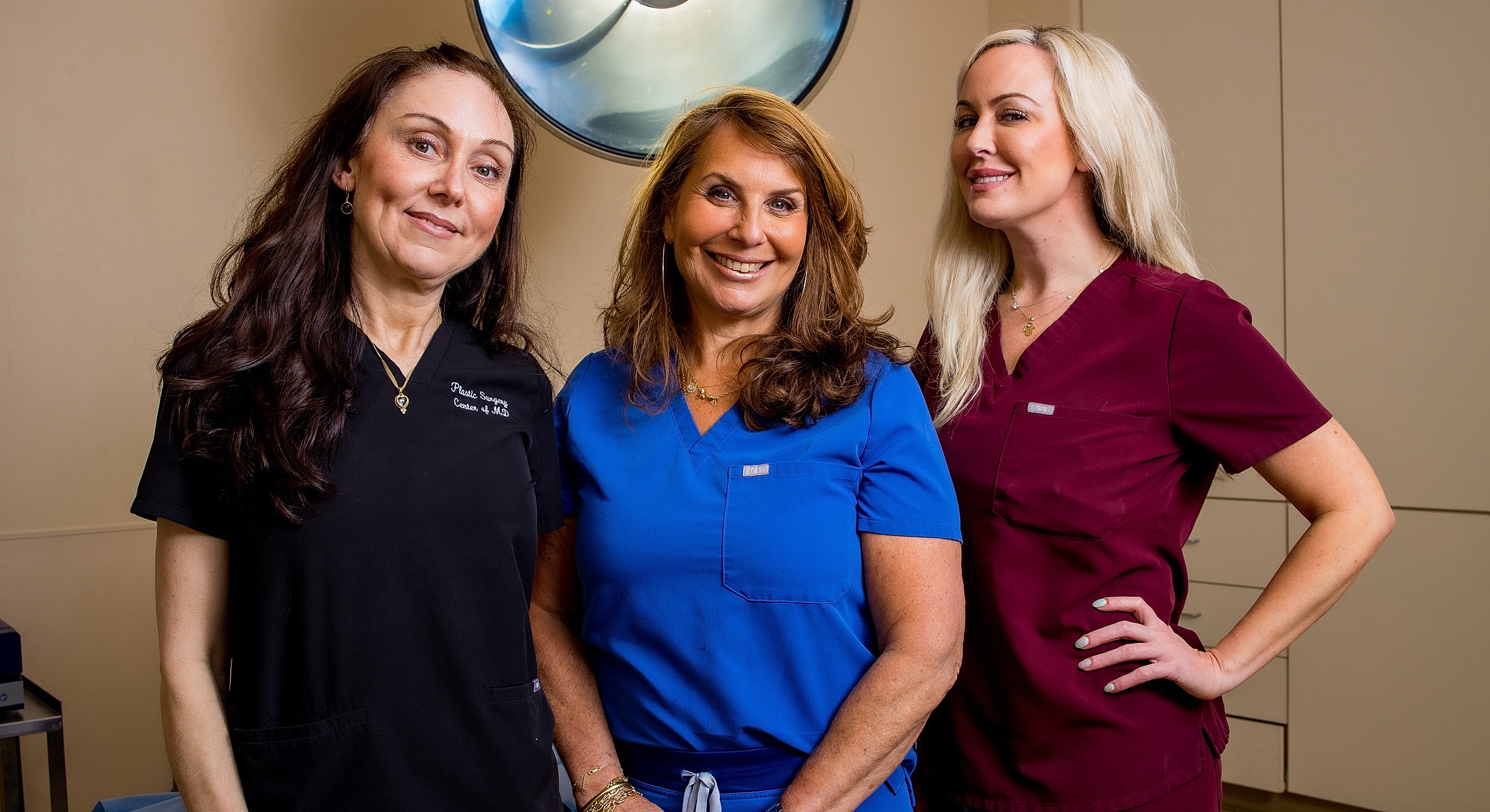Three women in medical scrubs smiling together.