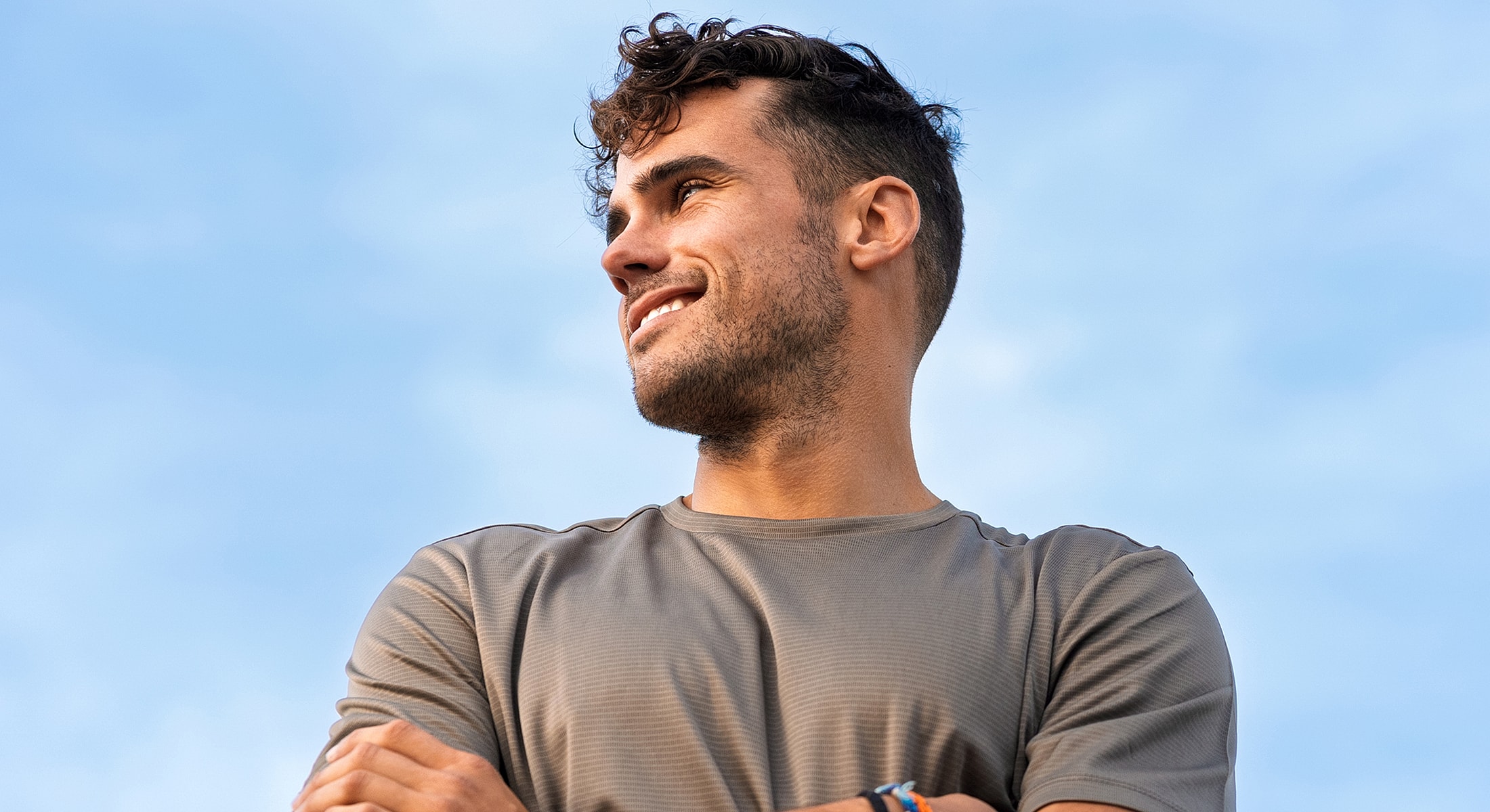 Smiling man looking upward against blue sky.
